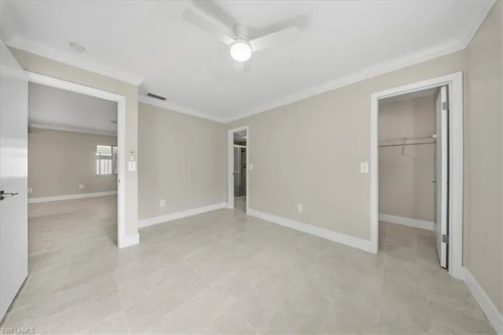 Unfurnished bedroom featuring a walk in closet, crown molding, and ceiling fan