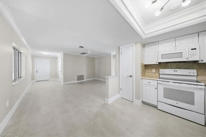 Kitchen with white appliances, ornamental molding, light countertops, white cabinetry, and backsplash