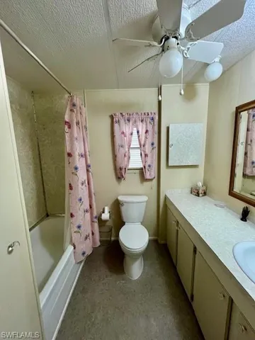 Bathroom featuring vanity, shower / tub combo with curtain, ceiling fan, and a textured ceiling