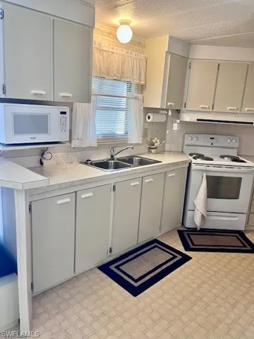 Kitchen with white appliances, range hood, light countertops, backsplash, and light floors