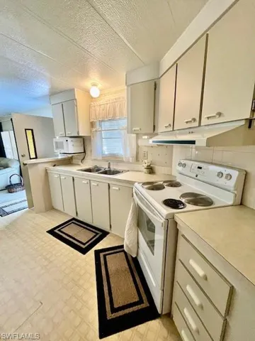 Kitchen with white appliances, under cabinet range hood, light countertops, and light flooring