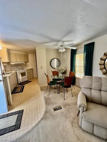Living area with a textured ceiling, a ceiling fan, and light carpet