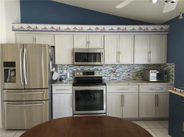 Kitchen featuring appliances with stainless steel finishes, decorative backsplash, light stone countertops, lofted ceiling, and ceiling fan