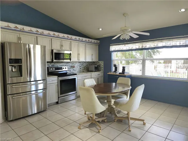 Kitchen featuring ceiling fan, light tile patterned floors, backsplash, appliances with stainless steel finishes, and vaulted ceiling