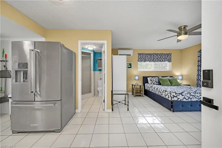 Bedroom with high end fridge, ensuite bath, a textured ceiling, ceiling fan, and an AC wall unit