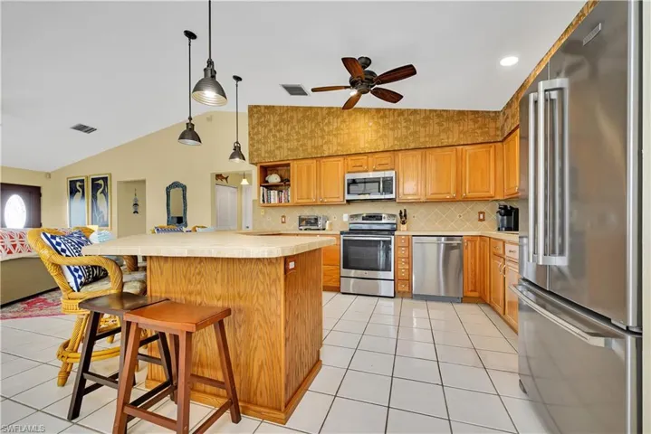 Kitchen featuring appliances with stainless steel finishes, lofted ceiling, a breakfast bar area, and light tile patterned floors