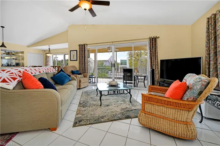 Living room with lofted ceiling, light tile patterned flooring, and ceiling fan