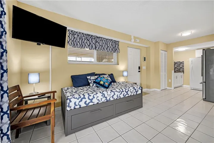 Bedroom with white refrigerator, a textured ceiling, stainless steel refrigerator, and light tile patterned flooring