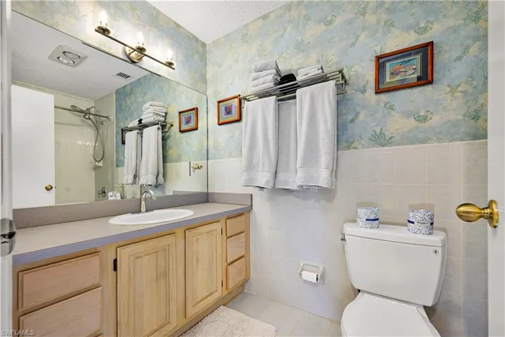 Bathroom with toilet, tile walls, a textured ceiling, a tile shower, and vanity