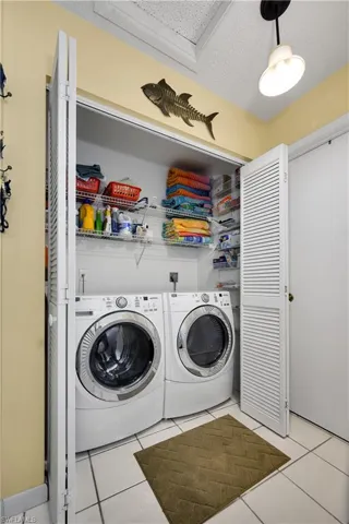 Laundry area with washing machine and clothes dryer, light tile patterned floors, and a textured ceiling