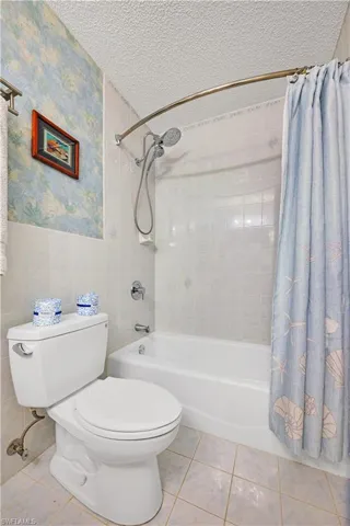 Bathroom featuring tile patterned flooring, a textured ceiling, toilet, and shower / tub combo with curtain