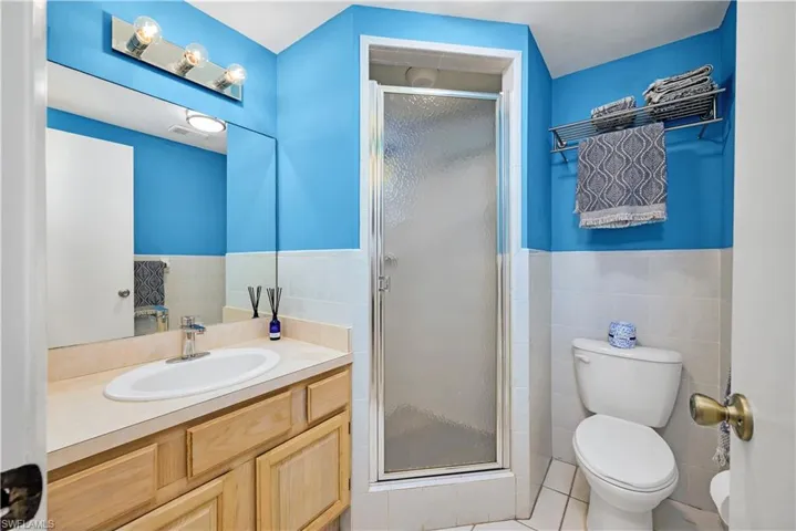 Bathroom featuring toilet, an enclosed shower, tile walls, and tile patterned floors
