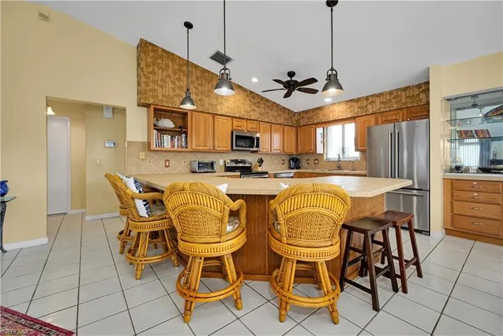 Kitchen featuring ceiling fan, light tile patterned flooring, a kitchen bar, and appliances with stainless steel finishes