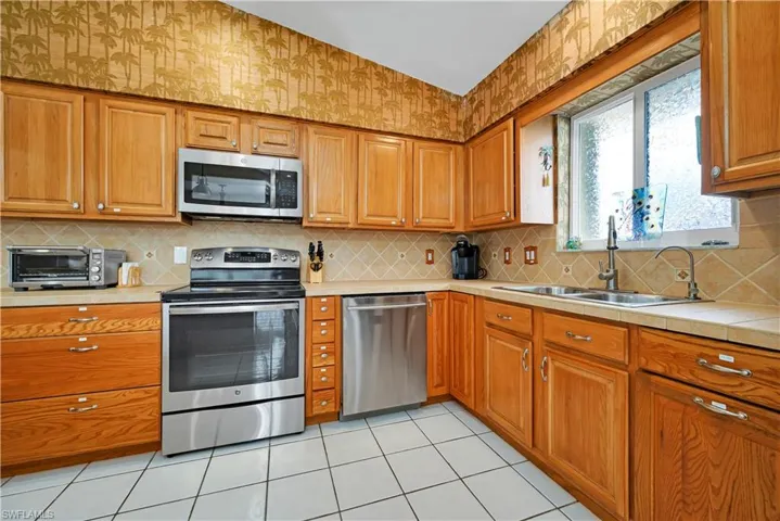 Kitchen featuring light tile patterned flooring, sink, appliances with stainless steel finishes, and tasteful backsplash
