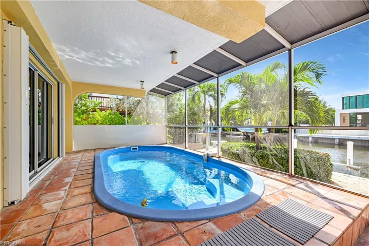 View of pool with a water view, glass enclosure, and a patio