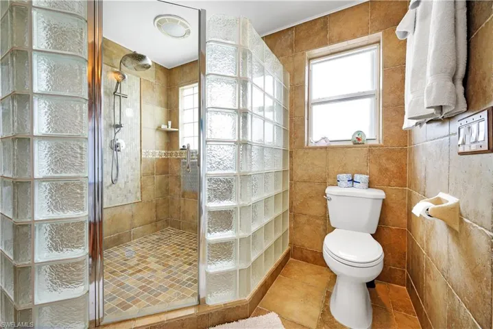 Bathroom with tile walls, a tile shower, toilet, and tile patterned floors