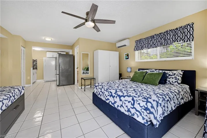 Bedroom with an AC wall unit, white fridge, light tile patterned flooring, a textured ceiling, and ceiling fan