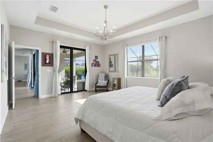 Bedroom featuring a tray ceiling, access to outside, multiple windows, light wood finished floors, and hanging lights