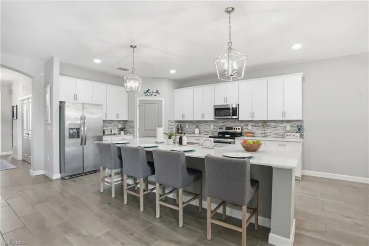 Kitchen with stainless steel appliances, a kitchen breakfast bar, light wood finished floors, and white cabinetry
