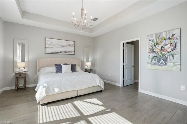 Bedroom with a chandelier, light wood-style floors, and a raised ceiling