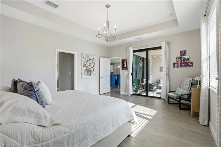 Bedroom with a raised ceiling, a chandelier, access to exterior, and light wood finished floors
