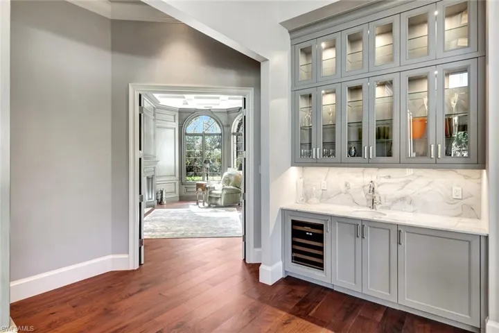 Bar featuring gray cabinetry, light stone countertops, sink, dark wood-type flooring, and crown molding