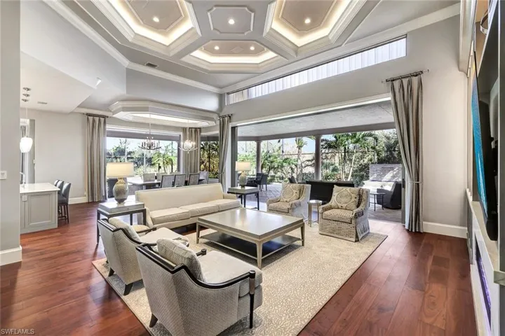 Living room featuring coffered ceiling, dark hardwood / wood-style floors, ornamental molding, a towering ceiling, and a notable chandelier