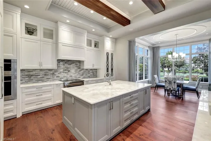 Kitchen with light stone countertops, dark hardwood / wood-style flooring, white cabinets, and a center island with sink