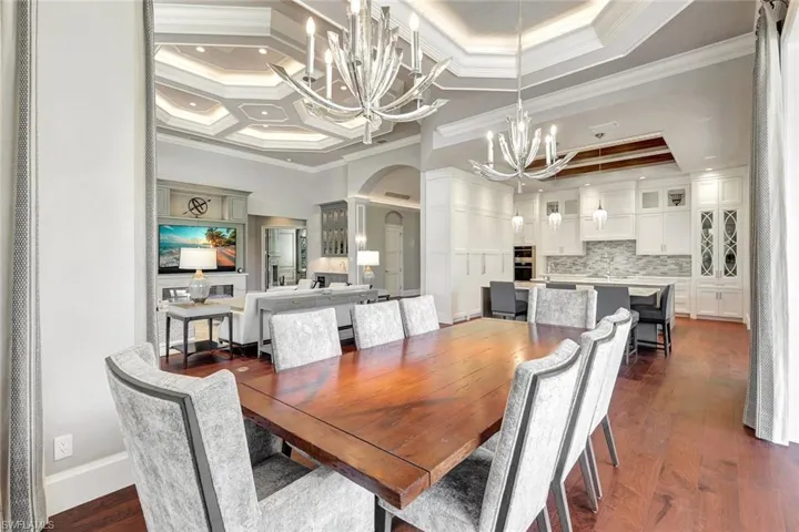 Dining area with coffered ceiling, a tray ceiling, dark wood-type flooring, crown molding, and a notable chandelier