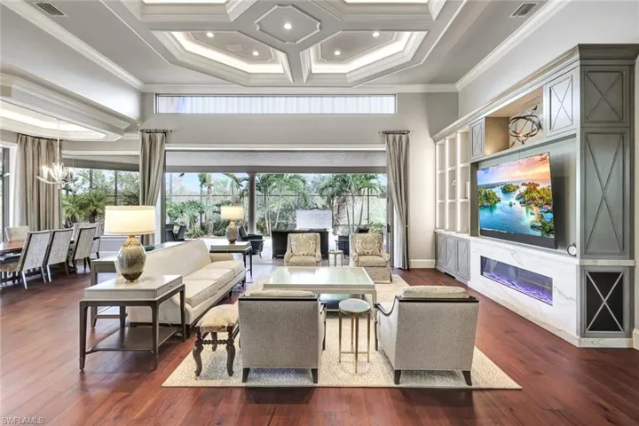 Living room with coffered ceiling, dark hardwood / wood-style floors, crown molding, and a chandelier