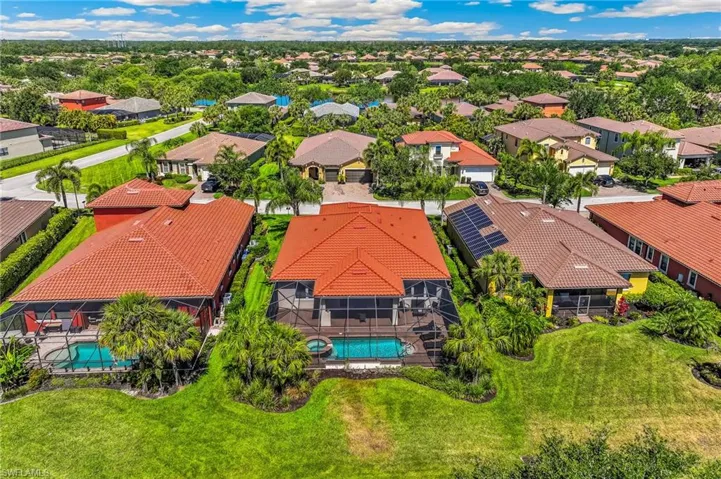 Residential property featuring a terracotta tile roof, screened lanai, inground pool, and surrounding mature landscaping