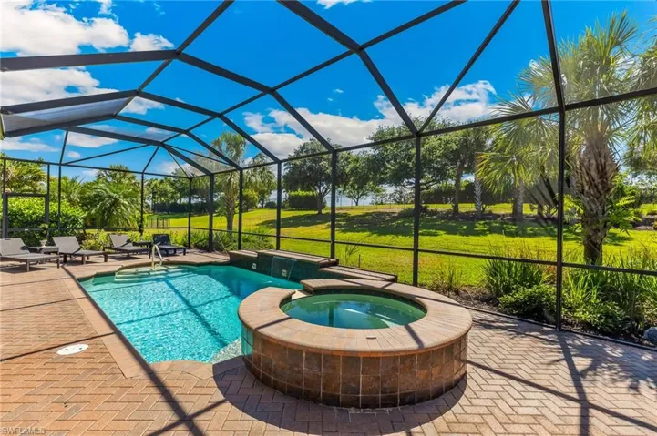 Screen-enclosed pool and spa area featuring brick paver decking, a rectangular pool with integrated steps, and a circular spa with tile surround