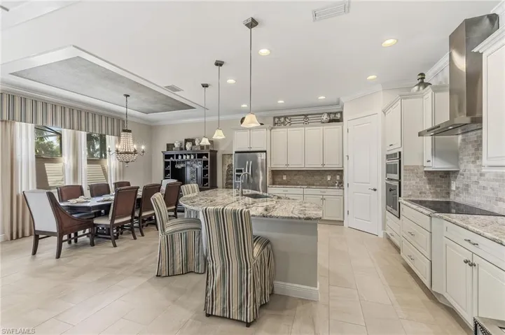 Spacious kitchen and dining area featuring light-toned tile flooring, recessed lighting, and a tray ceiling with a textured insert