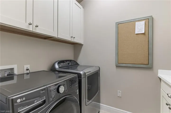 Laundry area featuring white cabinetry with silver hardware, neutral wall paint, light-colored baseboards, and a partial countertop with an integrated sink