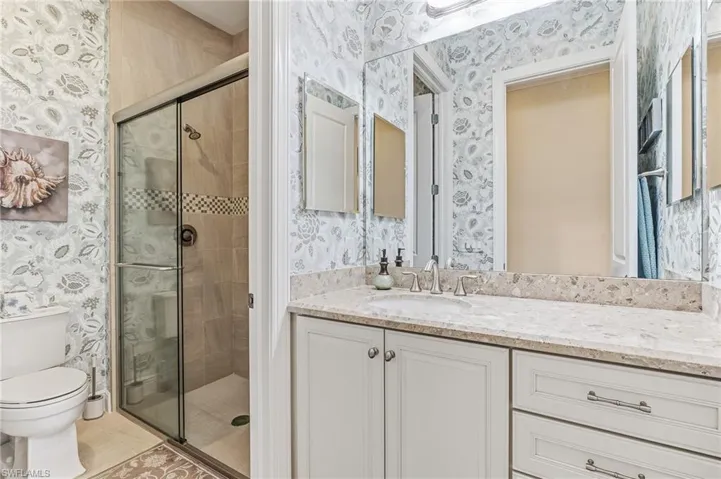 Bathroom featuring a built-in vanity with light-toned cabinetry and a light-toned countertop, an undermount sink with a chrome faucet, a large wall-mounted mirror, and a glass-enclosed shower with tiled walls and a decorative mosaic band