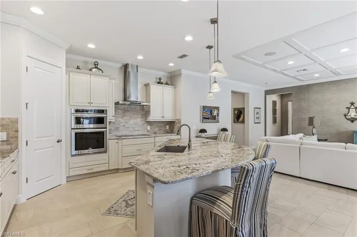 Modern kitchen featuring a curved island with stone countertop, pendant lighting, built-in stainless steel appliances, white cabinetry, and a tile backsplash