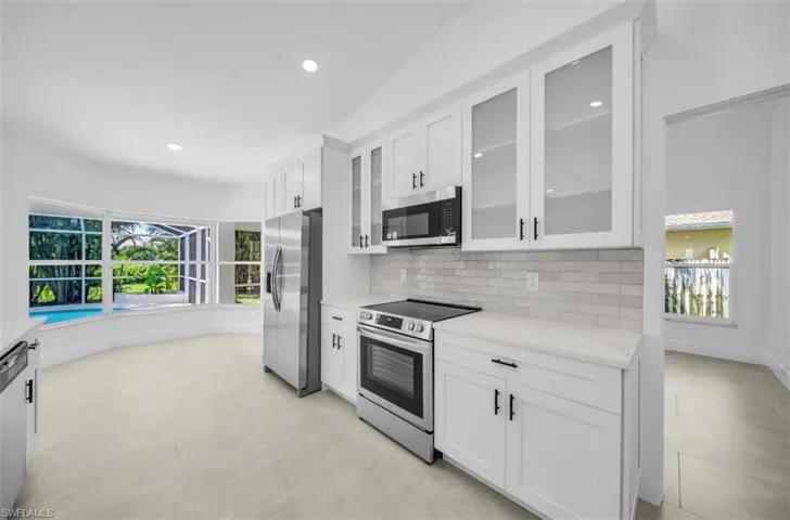 Kitchen featuring white cabinets, stainless steel appliances, glass insert cabinets, light stone countertops, and backsplash