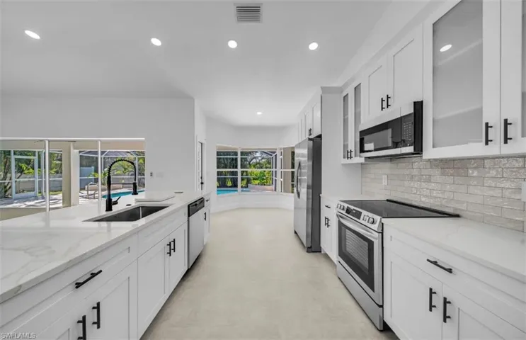 Kitchen featuring appliances with stainless steel finishes, white cabinetry, light stone counters, recessed lighting, and glass insert cabinets
