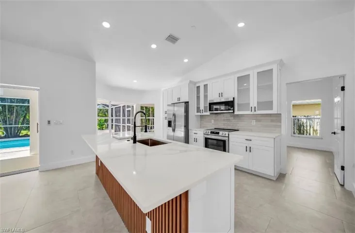 Kitchen featuring glass insert cabinets, white cabinetry, appliances with stainless steel finishes, decorative backsplash, and a large island