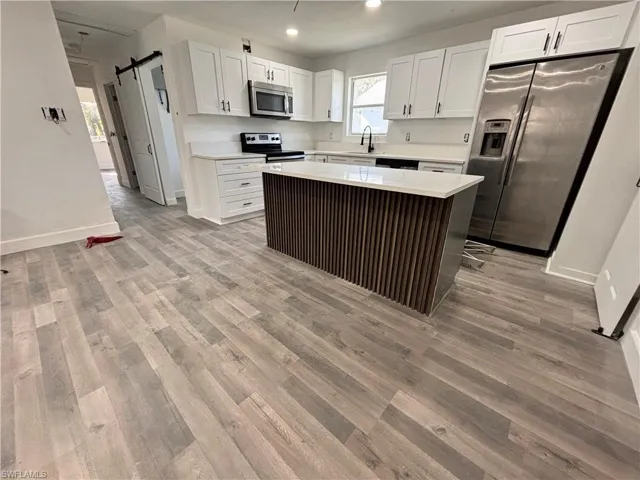 Kitchen featuring a barn door, white cabinets, appliances with stainless steel finishes, a center island, and light wood-type flooring