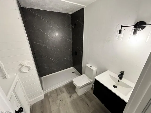 Bathroom featuring a marble finish shower, vanity, wood finished floors, and a textured wall