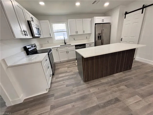 Kitchen featuring a barn door, appliances with stainless steel finishes, light wood-style flooring, white cabinets, and light stone countertops