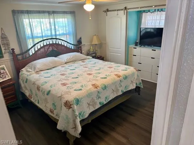 Bedroom with ceiling fan, a barn door, and dark hardwood / wood-style flooring