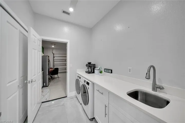 Washroom with light marble finish flooring, washer and dryer, and cabinet space