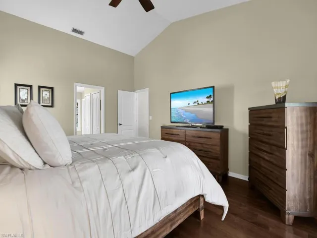 Bedroom with dark wood finished floors, high vaulted ceiling, ceiling fan, and ensuite bathroom