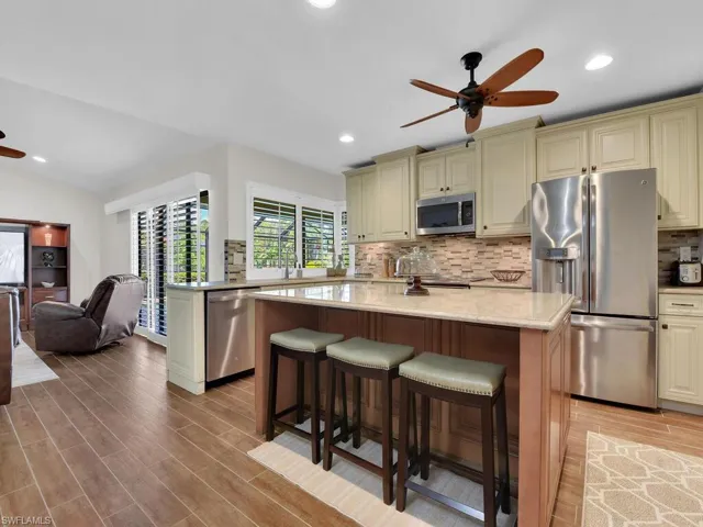 Kitchen with cream cabinetry, a breakfast bar, appliances with stainless steel finishes, wood finish floors, and light stone counters