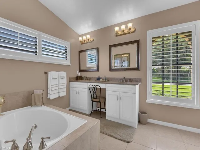Full bathroom featuring double vanity, tile patterned floors, a garden tub, and lofted ceiling