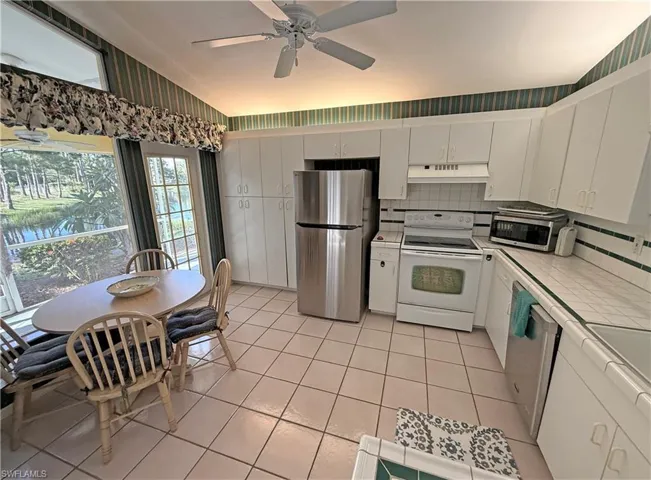 Kitchen with tile countertops, backsplash, appliances with stainless steel finishes, white cabinetry, and light tile patterned floors