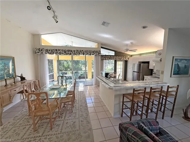 Dining area with vaulted ceiling, light tile patterned floors, track lighting, and a ceiling fan