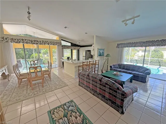 Living room featuring track lighting, lofted ceiling, light tile patterned floors, and a sunroom